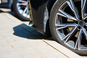 Close-up of a sleek black car parked on a sunlit brick pavement, focusing on its modern alloy wheel design and tire detail.